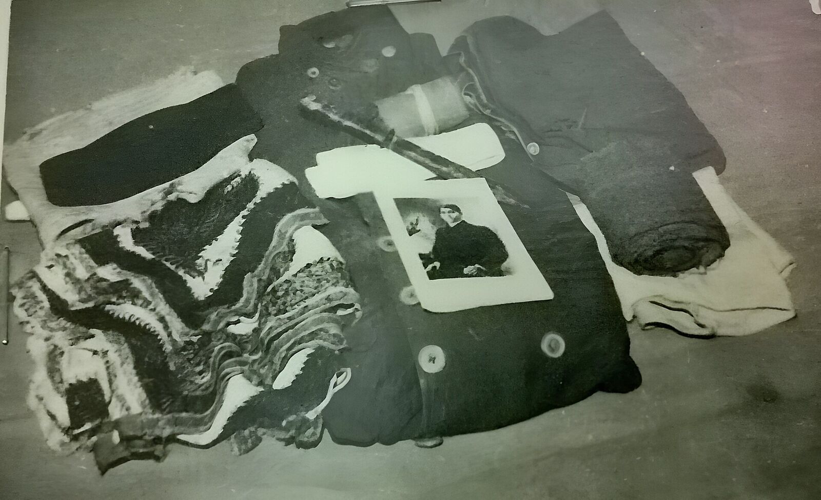 Folded garments and cloth laid out flat in a museum display, photographed from above, with a small portrait photograph resting on top.